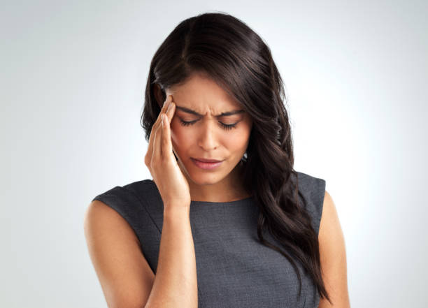 Shot of a young woman suffering from a headache while standing against a white background